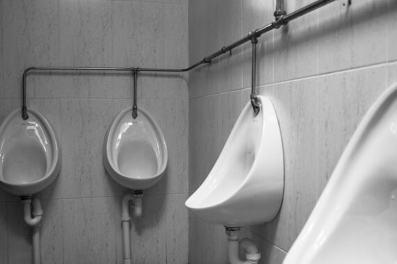 grayscale photography of four white ceramic urinal sinks