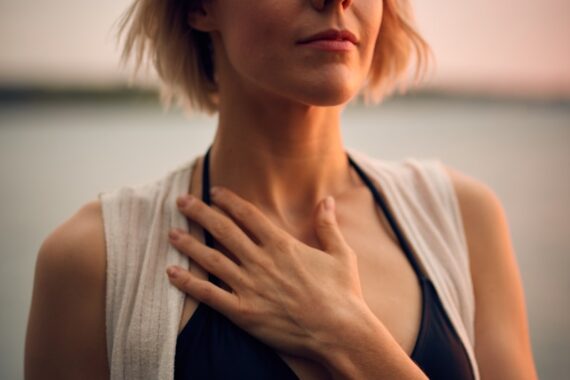 woman in white vest and black bikini with hand on chest