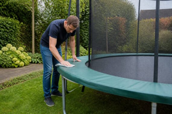Volwassene maakt het randkussen van een trampoline schoon in de tuin